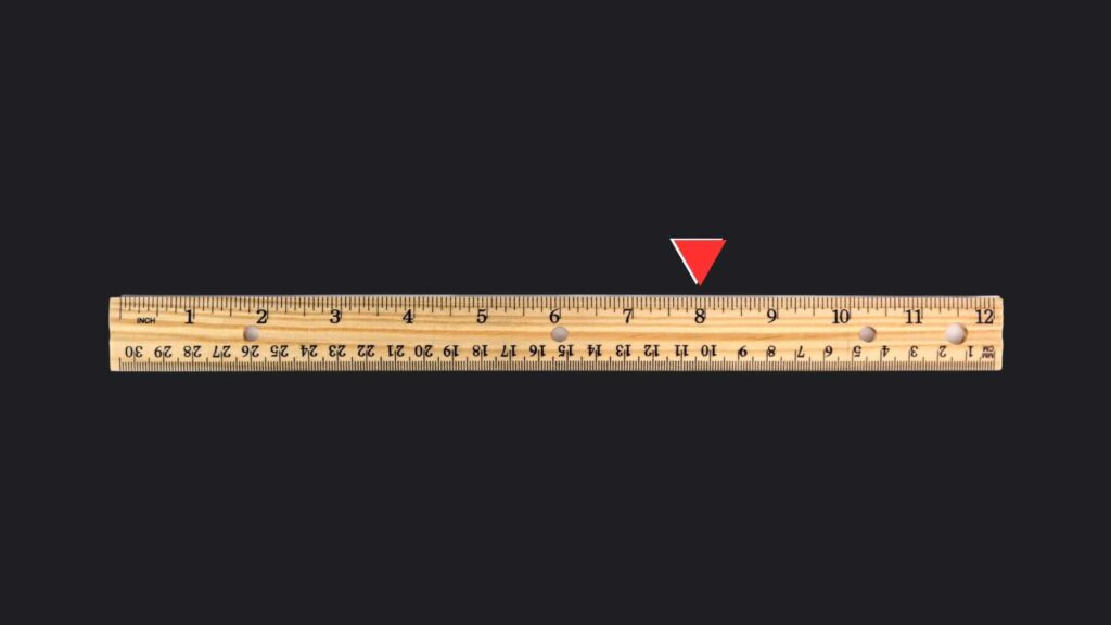 A standard wooden ruler placed on a black surface. The ruler is marked on the 8 inch with red triangle.