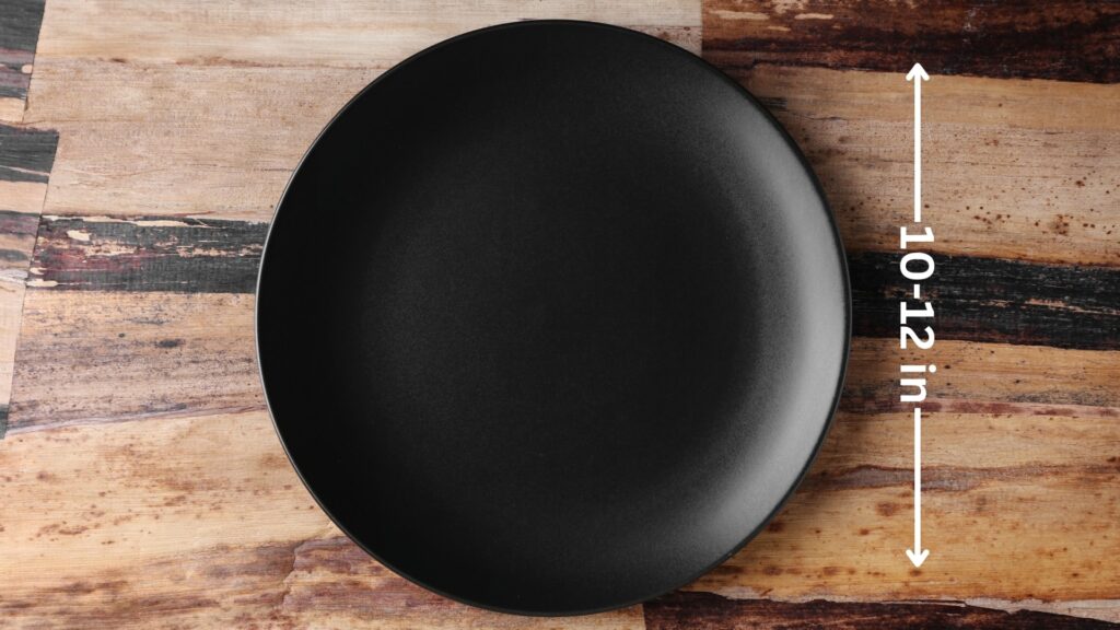 The image shows a black dinner plate placed on a wooden surface. The plate's diameter is marked with an annotation indicating a size range of 10 to 12 inches.